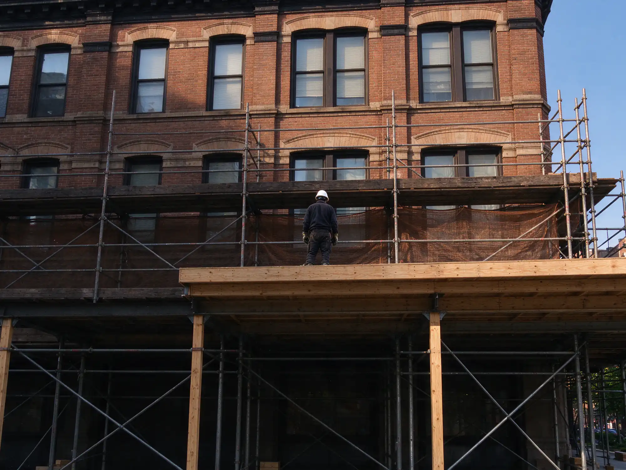 Prewar brick apartment building facade with scaffold and a covered sidewalk bridge